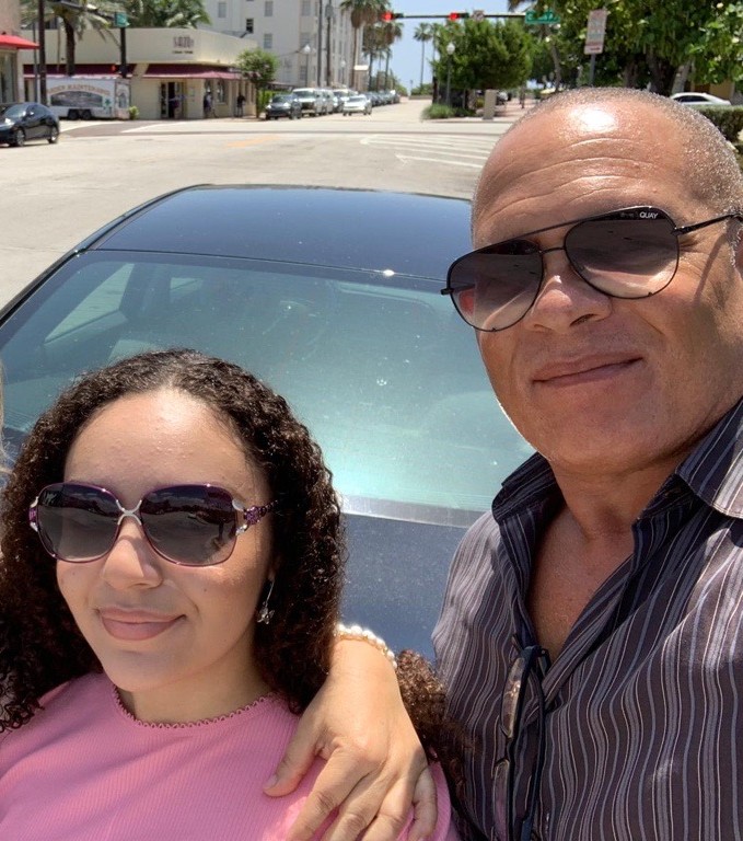Two people smiling in a busy city street with tall billboards behind them.